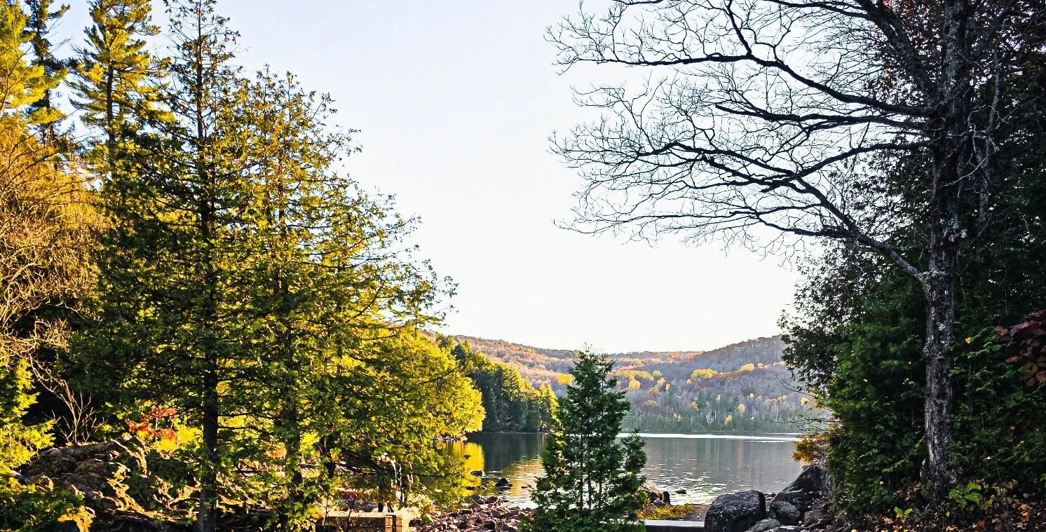 Autumn trees frame a quiet lake and rocky shoreline.
