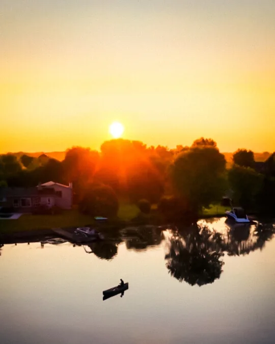 Sunset reflected in calm water with trees along the shore.